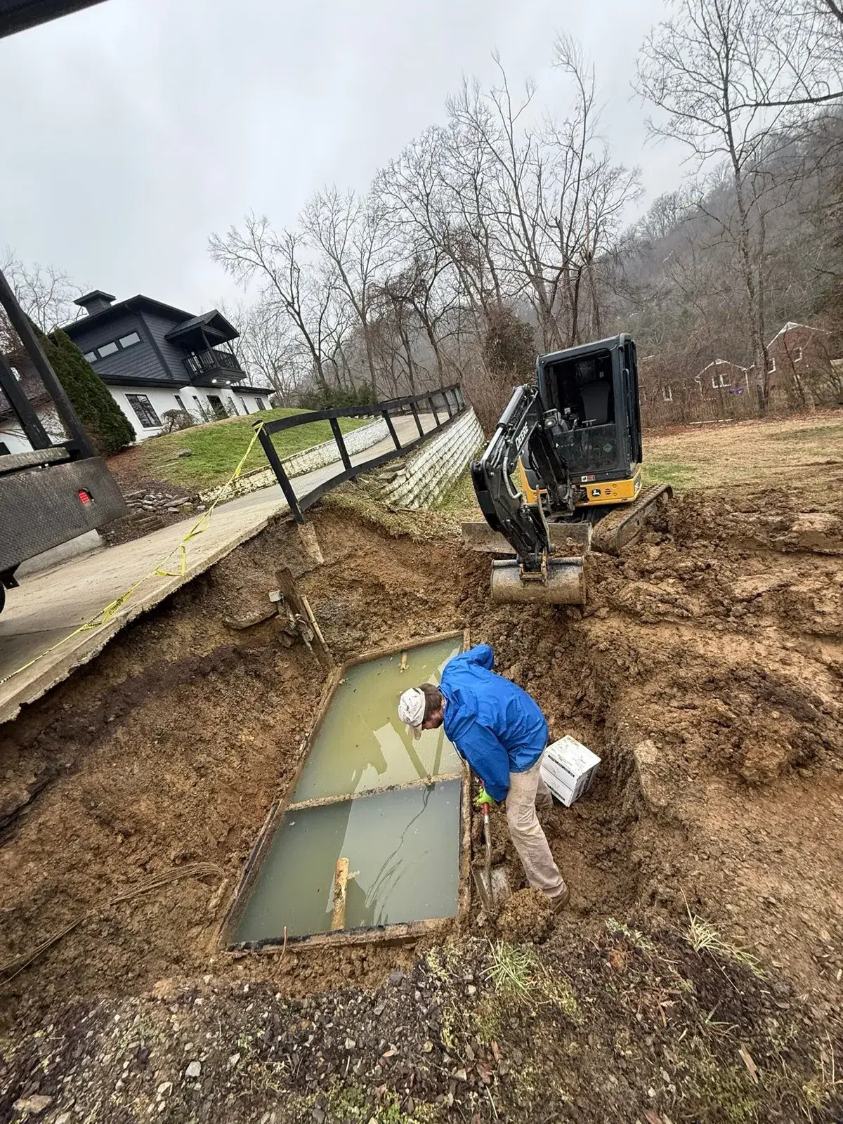 Crew setting a septic tank in an excavated pit beside a house
