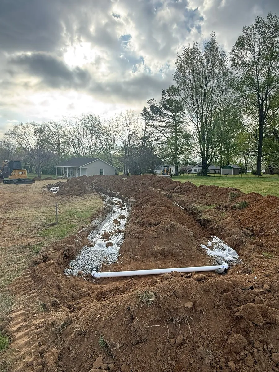 New drain field trenches with gravel beds and a white distribution pipe on a residential lot